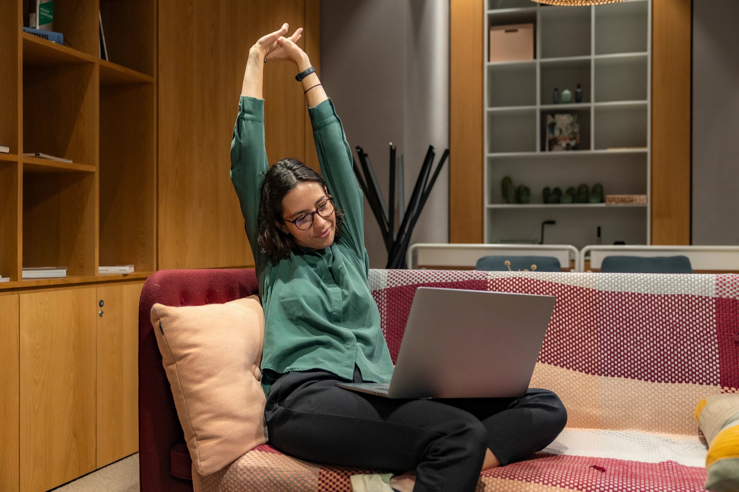 Mulher se espreguiçando no sofá com o notebook no colo