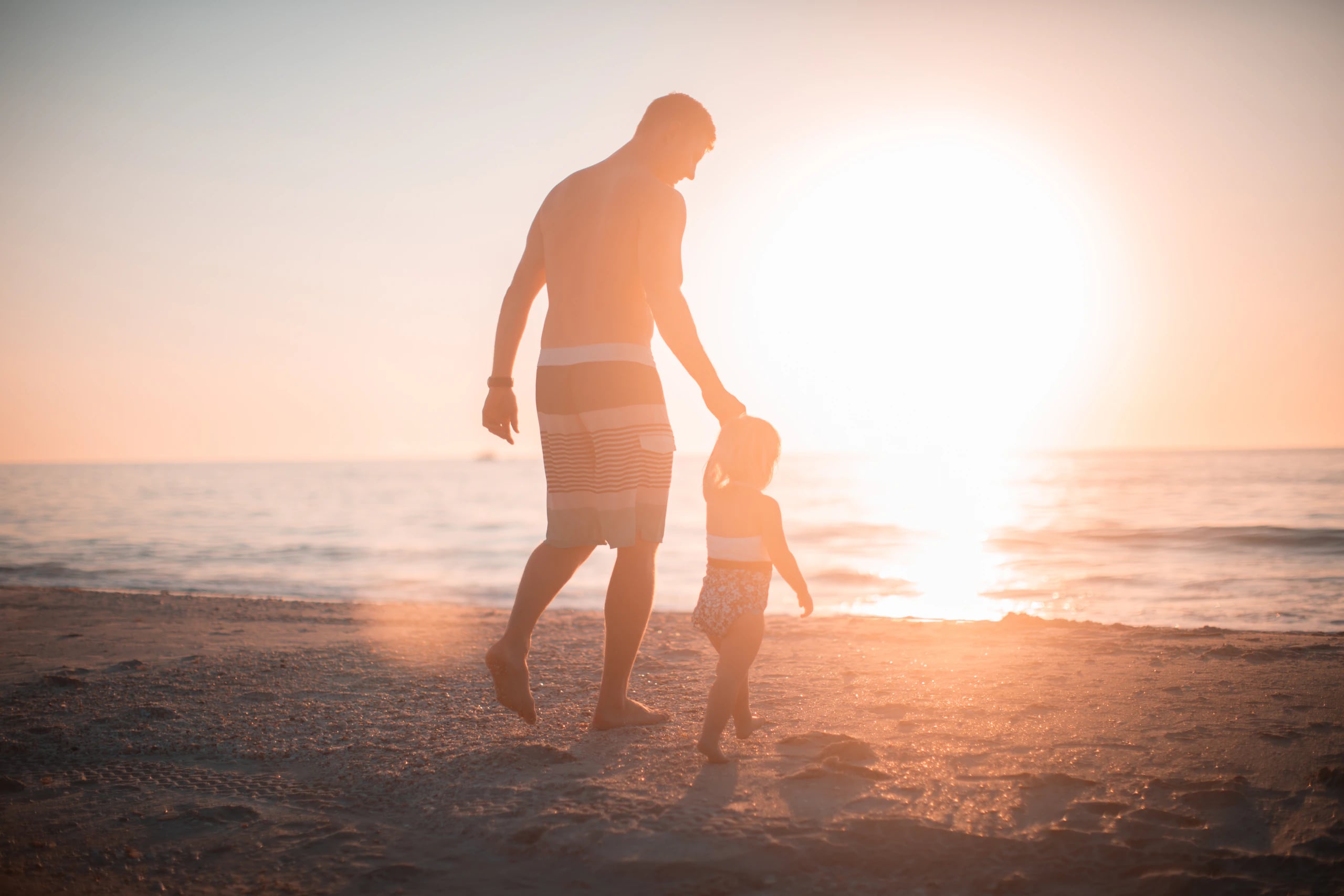 Pai e filho caminhando na praia ao pôr do sol
